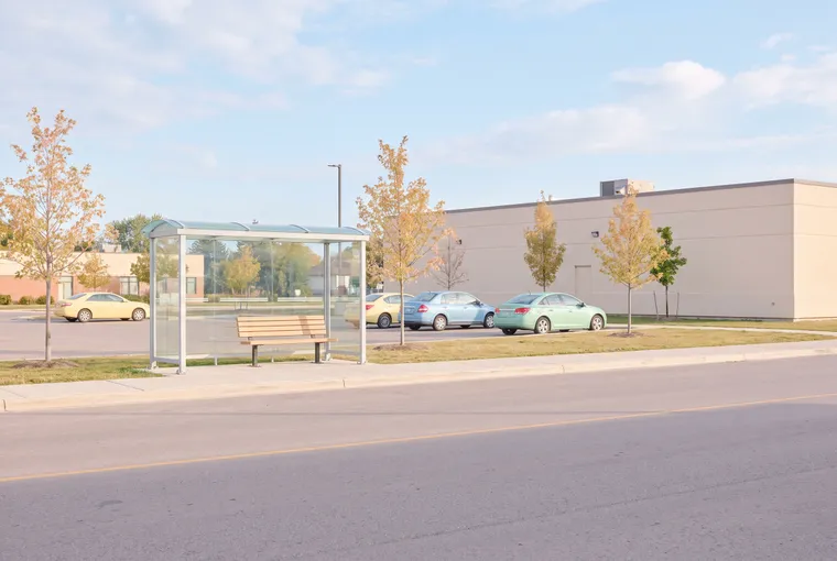 Illustration: an empty glass bus shelter by a wide, quiet road and a parking lot on a bright morning.